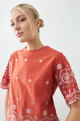 Remera de algodón color terracota con detalles de bordado broderie blanco en mangas y ruedo. Presenta cuello redondo y mangas cortas.