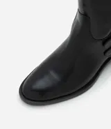 Bota de caña corta marca Satinato, confeccionada en poliuretano color negro. Presenta punta redondeada, taco bloque bajo y dos tiras decorativas con hebillas metálicas en el lateral externo.