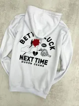 Canguro blanco con capucha, cordones ajustables y bolsillo tipo canguro. Estampado en el pecho con la frase "Better Luck Next Time" y un diseño de un corazón roto con una daga.