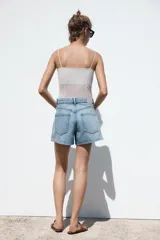 Shorts de jean color negro, tiro medio, corte mom fit, con cinco bolsillos, cierre frontal con cremallera y botón.