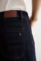 Pantalón de jean azul oscuro con corte flare, tiro alto y bolsillos delanteros tipo plaqué. Presenta costuras a la vista y una silueta amplia en las piernas.