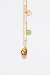 Collar de doble cadena, una de perlas irregulares y otra de eslabones dorados con pequeñas bolitas. La cadena dorada tiene dijes colgantes en forma de corazón esmaltados en varios colores (marrón, vino, verde menta, rosa pálido). El cierre es tipo toggle dorado.