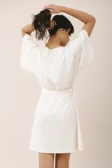 Bata corta color crema, confeccionada en algodón con elastano, con escote en V, mangas anchas y lazo para ajustar en la cintura.