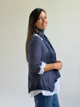 Sweater de punto azul con diseño asimétrico y detalles bordados, que incluye una bufanda a juego y una camisa blanca de lino debajo.