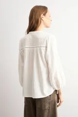 Blusa blanca de corte holgado con cuello mao y escote en V. Presenta detalles de bordado calado en el pecho y en los puños de las mangas tres cuartos.