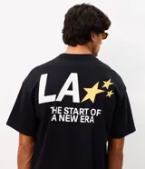 Remera de corte oversized confeccionada en mezcla de algodón y poliéster. Presenta cuello redondo, mangas cortas con hombros caídos y diseño estampado en la espalda con la frase 'LA THE START OF A NEW ERA' acompañada de estrellas amarillas.