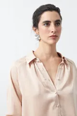 Camisa negra de corte relajado y caída fluida, con cuello clásico, escote en V y cierre frontal con botones forrados. Presenta mangas largas con puños abotonados.