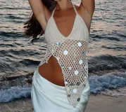 Top halter tejido al crochet color crudo, con escote en V y espalda descubierta. Presenta una abertura lateral y está decorado con lentejuelas plateadas.