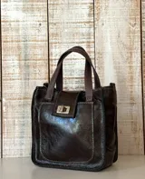 Mini bag de cuero marrón oscuro, con doble asa de mano y bolsillo frontal con cierre metálico giratorio.