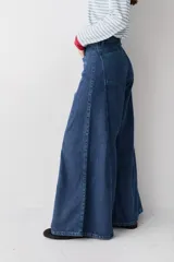 Jean de corte wide leg con tiro alto, confeccionado en denim azul oscuro. Presenta costuras verticales a lo largo de las piernas con pespuntes en color verde a contratono.