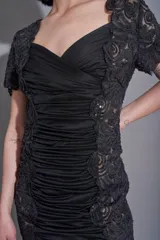 Vestido negro de corte recto, con cuello cruzado, mangas cortas de encaje con bordados y laterales de encaje con bordados.