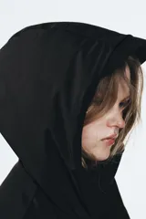 Chaqueta acolchada de corte corto con cuello subido y capucha. Presenta cierre frontal con cremallera termosellada y solapa con botones a presión, bolsillos laterales con cierre, mangas largas con puños elásticos y bajo ajustable con cordones.