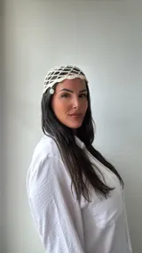 Gorro de crochet color crudo con diseño de red y dije plateado colgando.