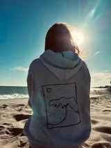Hoodie gris con capucha y cordón ajustable, corte oversize y estampa en la espalda de una ola dentro de un recuadro.