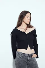 Top de punto acanalado negro, con diseño off-shoulder y escote amplio. Presenta mangas largas y cierre frontal completo con doble cursor, permitiendo ajustar la apertura superior e inferior.