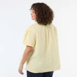 Blusa de gasa de algodón color amarillo pastel, con cuello alto fruncido, cierre frontal parcial con botones y mangas cortas abullonadas.