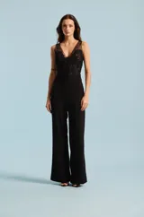 Mono largo negro sin mangas, con escote en V y cuerpo superior de tul transparente con apliques de encaje bordado. Pantalón de corte recto y tiro alto.
