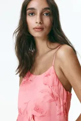 Vestido corto de gasa liviana rosado con estampado floreado, escote redondo pronunciado y breteles finos ajustables. Presenta un volado asimétrico amplio en la cintura y bajo asimétrico.