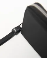 Billetera negra de símil cuero con cierre perimetral y parche circular con el logo de la marca en relieve en el centro.