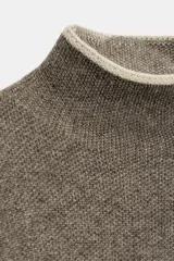 Jersey de punto con cuello subido y manga larga, de corte holgado. Presenta detalles de vivos en color crema en el cuello, puños y costuras de las mangas, contrastando con el tono marrón jaspeado de la prenda.