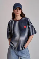 Remera oversize a rayas horizontales en tonos bordó y blanco, con cuello redondo verde oscuro y un pequeño parche bordado en forma de corazón en el pecho.