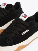 Zapatillas Tommy Jeans de corte bajo, color negro, con exterior de ante, interior de poliéster y suela de goma color caramelo. Presentan un panel a contraste en el talón, logo de Tommy Jeans en la lengüeta y etiqueta de la marca en el lateral.
