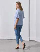 Blusa celeste y blanca a rayas verticales, de lino y corte holgado. Tiene cuello redondo con escote en V y lazo de ajuste. Las mangas son cortas y amplias, con volados en el borde.