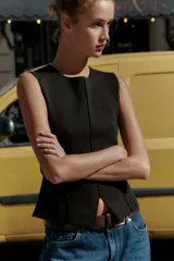 Top negro de punto, sin mangas, con cuello redondo. Presenta costuras marcadas en el frente y un bajo con abertura frontal que simula un peplum ajustado.