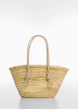 Bolso tipo shopper de fibra natural de hoja de palma, con diseño trenzado y detalles en piel bovina. Cuenta con dos asas largas con nudos decorativos y cierre de gancho.