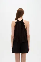 Top blanco de algodón con cuello halter, diseño holgado y detalle de encaje en el borde inferior.