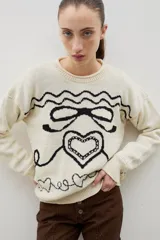 Buzo de cuello redondo con calce holgado, confeccionado en tejido de punto grueso con diseño jacquard de moña y corazones en contraste.