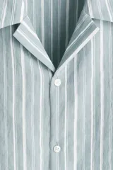 Camisa de manga corta con cuello abierto (cubano) y tapeta lisa, confeccionada en tejido suave de mezcla de lyocell. Presenta un patrón de rayas verticales blancas sobre un fondo verde menta o celeste pálido.