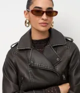 Campera estilo biker de cuero sintético color negro, con cuello solapa, cierre frontal asimétrico, bolsillos laterales con cremallera y detalles de botones metálicos en hombros y solapas.