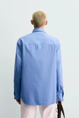 Camisa de corte regular fit confeccionada en tejido de algodón de color azul. Cuenta con cuello solapa, manga larga con puño abotonado, bolsillo de parche en el pecho y cierre frontal con botones.