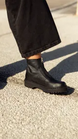 Bota corta de cuero negro con cierre frontal y suela track dentada. Diseño de caña baja con costuras reforzadas y forro interior de felpa.