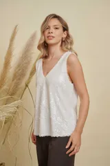 Musculosa de lentejuelas color blanco, con doble escote en V tanto en el frente como en la espalda, breteles anchos y diseño levemente acampanado.