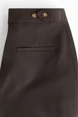 Pantalón de corte holgado en sarga color marrón oscuro. Modelo de tiro alto con trabilla ajustable de botón a ambos lados de la pretina, cierre con corchete oculto, piernas barrel con pinzas, pliegues adelante y atrás, bolsillos al bies y bolsillos traseros decorativos.