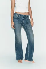 Jeans de tiro bajo con corte bootcut, confeccionados en denim con efecto lavado. Presentan costuras verticales marcadas en el frente, cierre frontal con cremallera, gancho metálico y detalle de trabilla con botones en la cintura.
