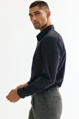 Camisa de tela azul marino con tratamiento de fácil planchado. Modelo Slim Fit con cuello inglés, tapeta clásica, canesú en la espalda, mangas largas con tapeta y botón, y puños ajustables con botón. Bajo ligeramente redondeado.