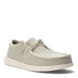 Zapatos tipo slip-on de tela color beige, con diseño de costuras expuestas, cordones elásticos decorativos y suela de goma blanca.