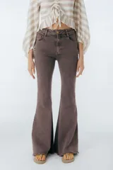 Pantalón de jean azul oscuro, corte acampanado (flare) de tiro alto, con costuras visibles en contraste y bordados tonales en la parte inferior de las piernas. El ruedo es deshilachado.