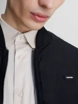 Chaleco negro acolchado con cuello alzado, cierre de cremallera, bolsillos con botón a presión y logo de Calvin Klein en el pecho.
