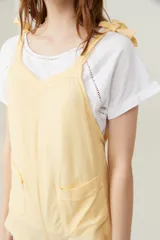 Mono corto color amarillo pastel, con breteles finos que se atan en los hombros, escote recto y dos bolsillos delanteros.