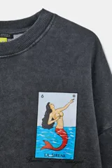 Sudadera de cuello redondo y manga larga con acabado efecto lavado en color gris oscuro. Presenta un pequeño estampado frontal con la ilustración de la carta de lotería La Sirena de Don Clemente.