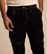 Pantalón masculino modelo baggy confeccionado en sarga de algodón, con cintura con trabillas, bolsillos cargo laterales y costuras con pespuntes en contraste.