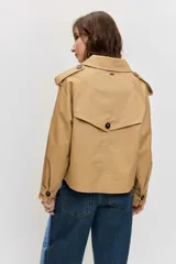 Cazadora corta de estilo gabardina en color tostado, con diseño cruzado de doble botonadura, solapas amplias, mangas largas con trabillas en los puños y hombreras.