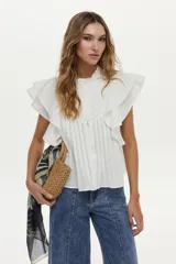 Blusa blanca sin mangas, con volados amplios en los hombros, bordado a tono en el pecho, detalles de tablones a lo largo del cuerpo y cuello elevado con volados.