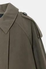 Trench corta verde militar con capucha, cuello solapa y manga larga con trabillas en los puños. Presenta bolsillos delanteros de vivo y cierre frontal cruzado con doble botonadura.