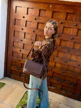 Cartera bandolera de cuero color chocolate con solapa frontal, costuras a la vista y herrajes metálicos. Incluye dos correas desmontables, una corta y una larga, y cuenta con bolsillo interior.