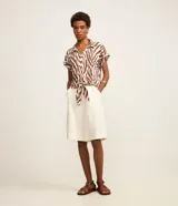 Blusa de manga corta confeccionada en viscosa, con cuello camisero, cierre frontal con botones y detalle de lazo para anudar en el bajo. Presenta un estampado híbrido entre follaje y animal print de cebra en tonos marrón y blanco.